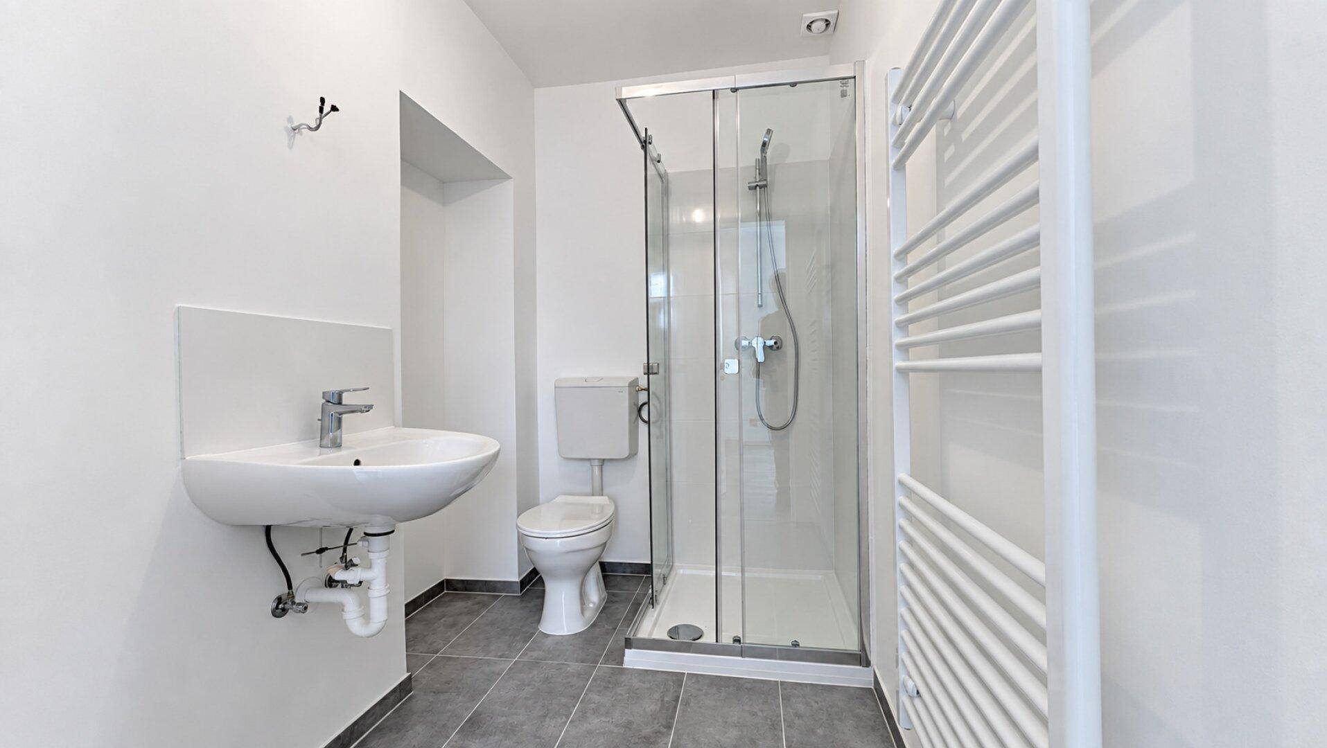 Modernes Badezimmer mit Duschkabine, WC, Waschbecken und einem praktischen Handtuchheizkörper.