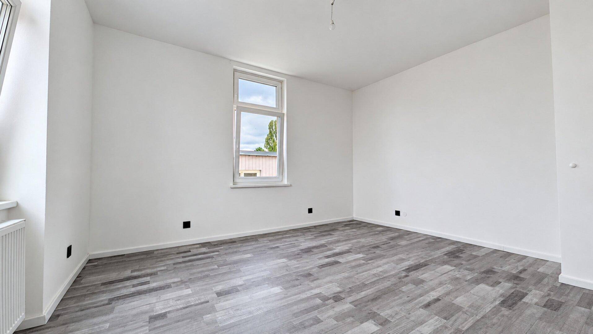 Heller, leerer Raum mit modernem Laminatboden und einem Fenster, ideal zur individuellen Nutzung.