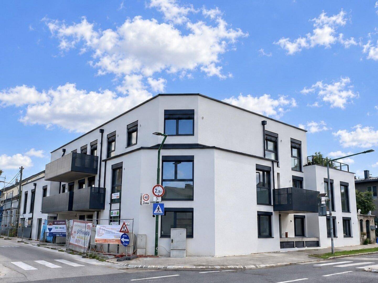 Eckgebäude mit moderner weißer Fassade, schwarzen Fenstern und Balkonen, noch im Bauzustand.