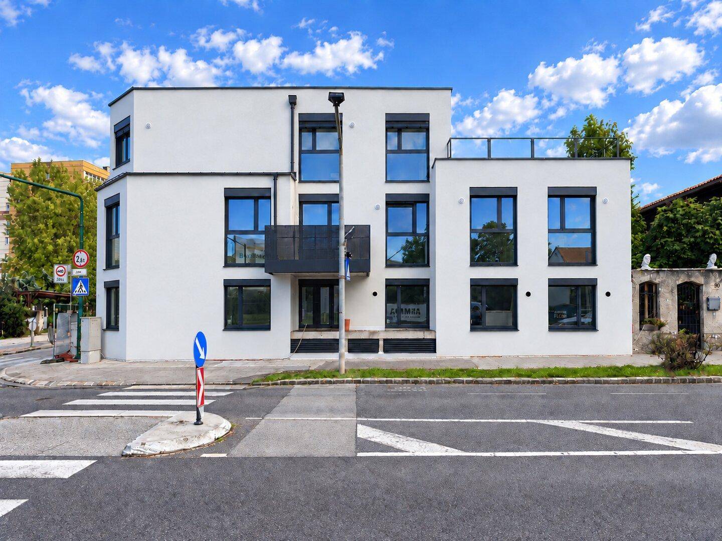 Modernes Wohngebäude mit weißer Fassade, großen Fenstern und einer Dachterrasse.