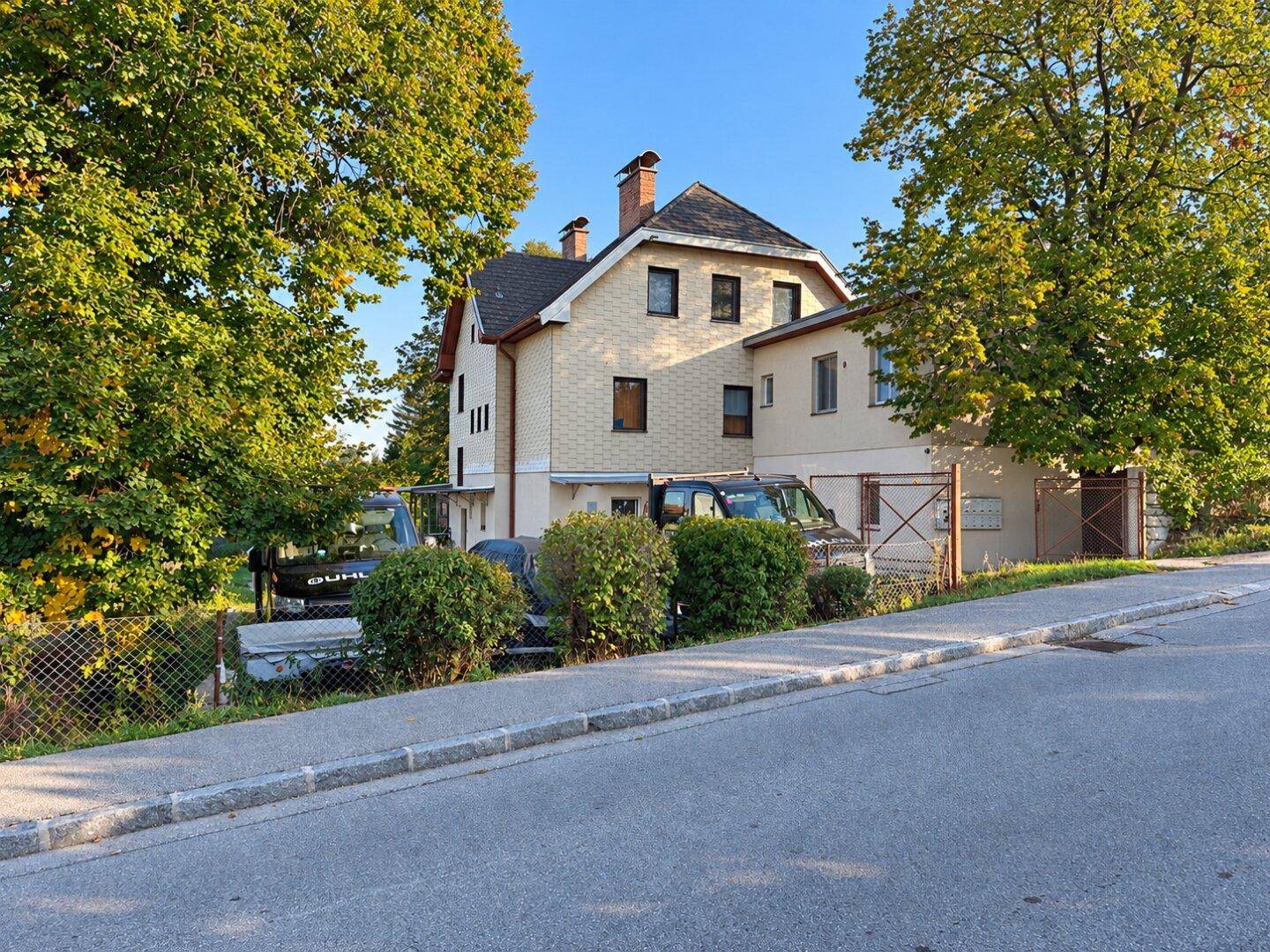 Seitenansicht des Hauses von der Straße aus, umgeben von Bäumen und Grünflächen.