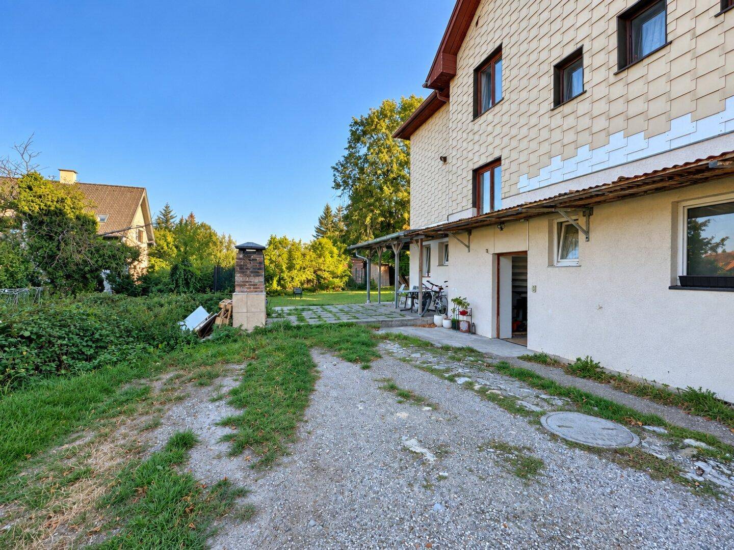 Überdachter Terrassenbereich am Haus mit Zugang zum Garten und gemauertem Grill.