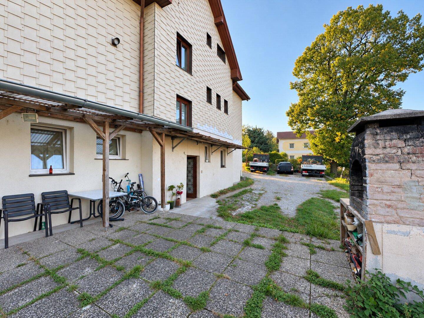 Gepflasterte Terrasse mit Sitzgelegenheiten, Fahrrädern und einem traditionellen Grillofen.