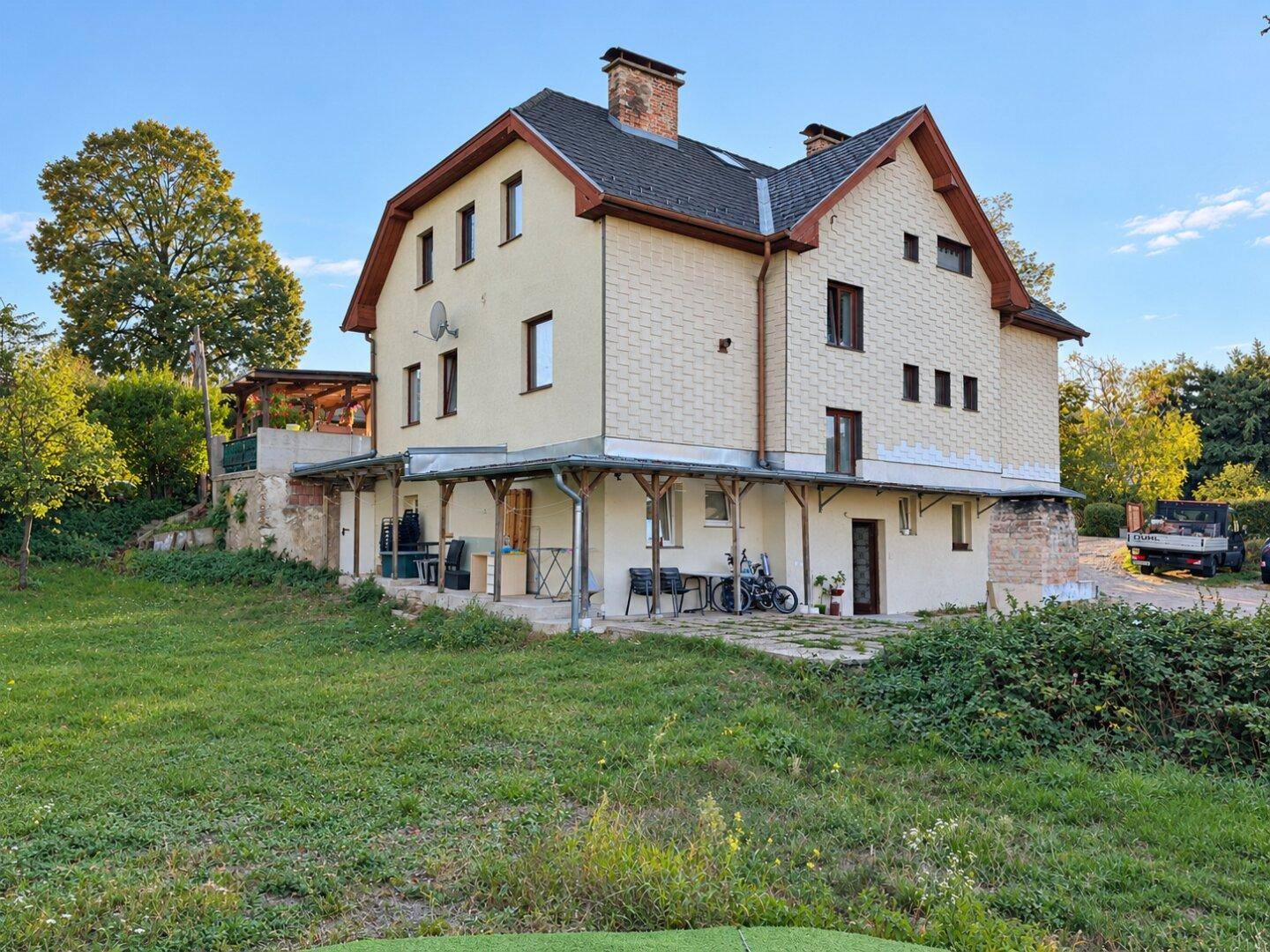 Rückseite des Hauses mit weitläufigem Rasenbereich und überdachter Terrasse im Vordergrund.