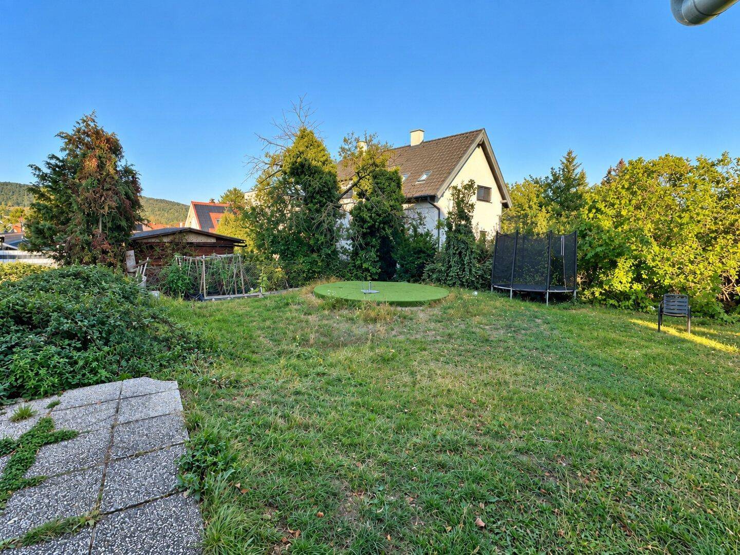 Gartenbereich mit Trampolin, kleinem Putting-Green und umgebenden Grünflächen.