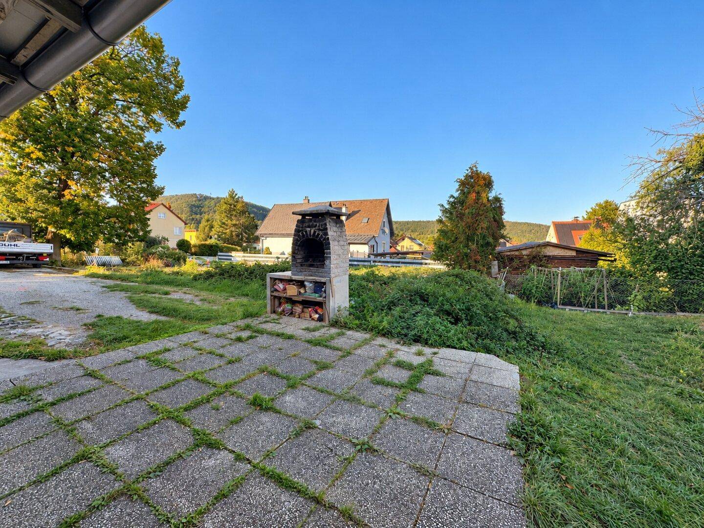 Gepflasterter Terrassenbereich mit gemauertem Grill und weitem Blick in den Garten.