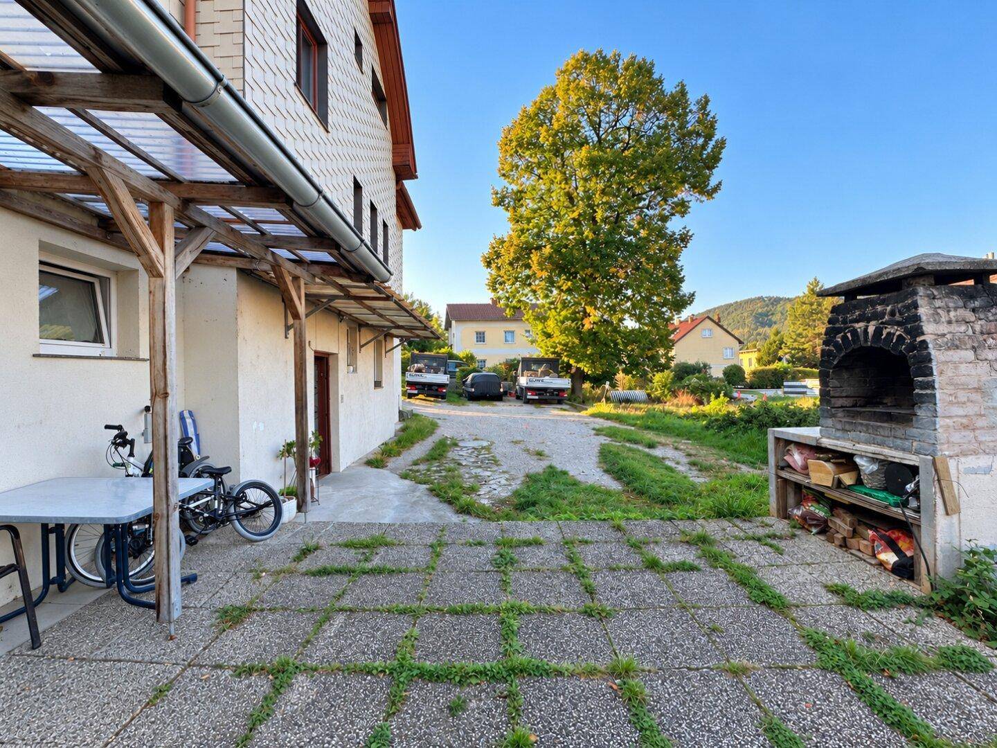 Überdachte Terrasse mit Sitzgelegenheiten und einem traditionellen Steinofen-Grill im Freien.