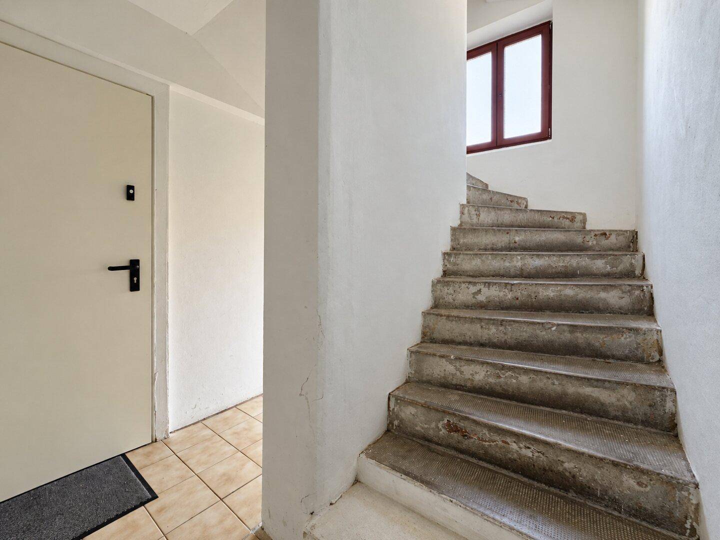Treppenhaus mit Steinstufen, weiß gestrichenen Wänden und einem Fenster für Tageslicht.