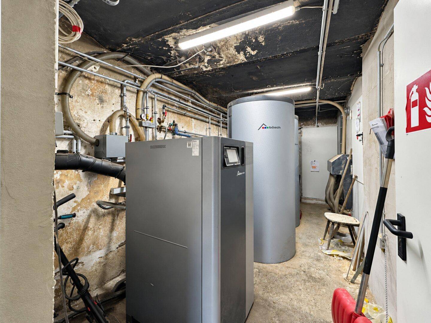 Heizungsraum mit modernen Heizungsanlagen, Warmwasserspeichern und sichtbaren Rohren.