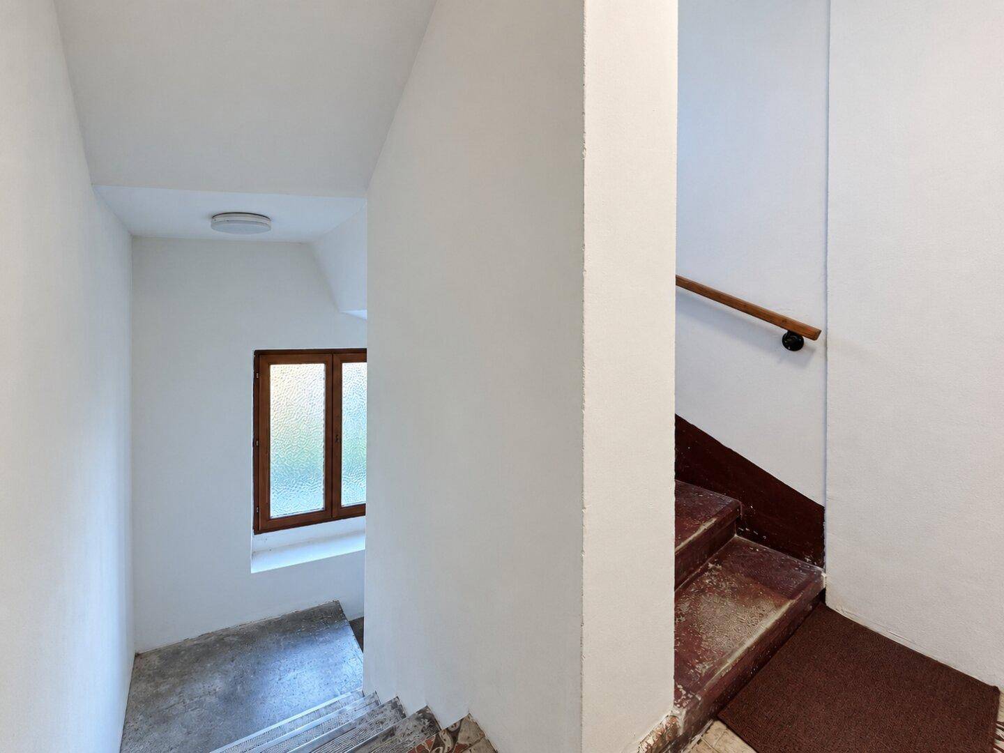 Treppenaufgang mit Holzgeländer und einem Fenster, das den Blick nach unten freigibt.