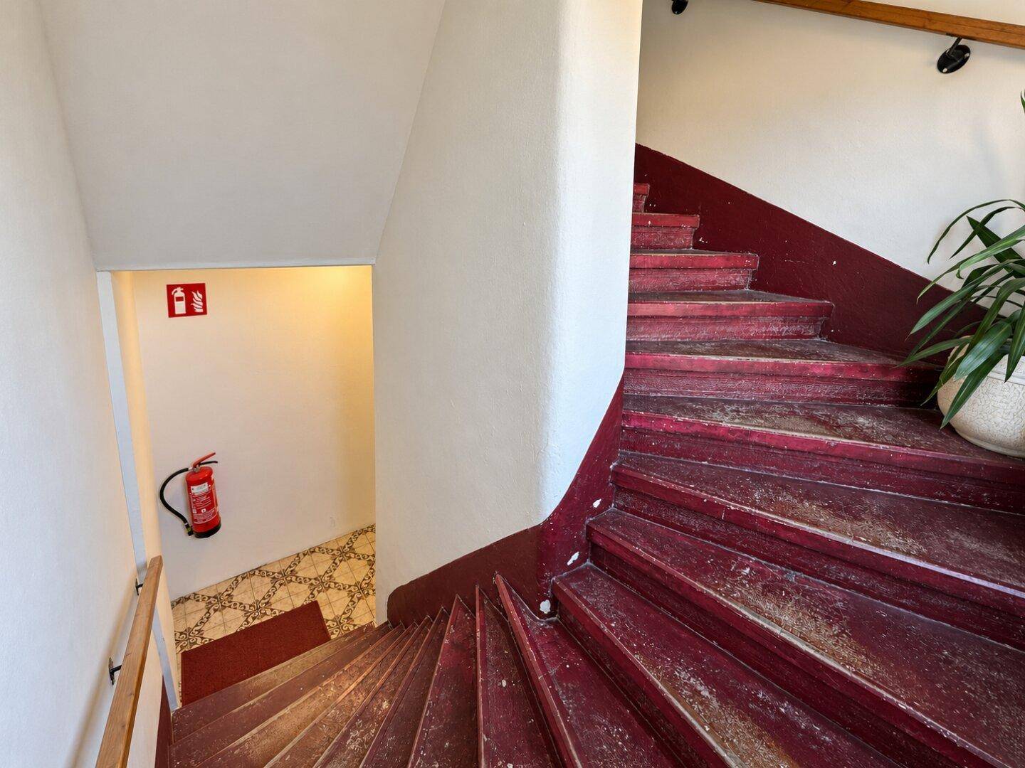 Treppenhaus mit roten Stufen, weiß gestrichenen Wänden und einem Feuerlöscher.