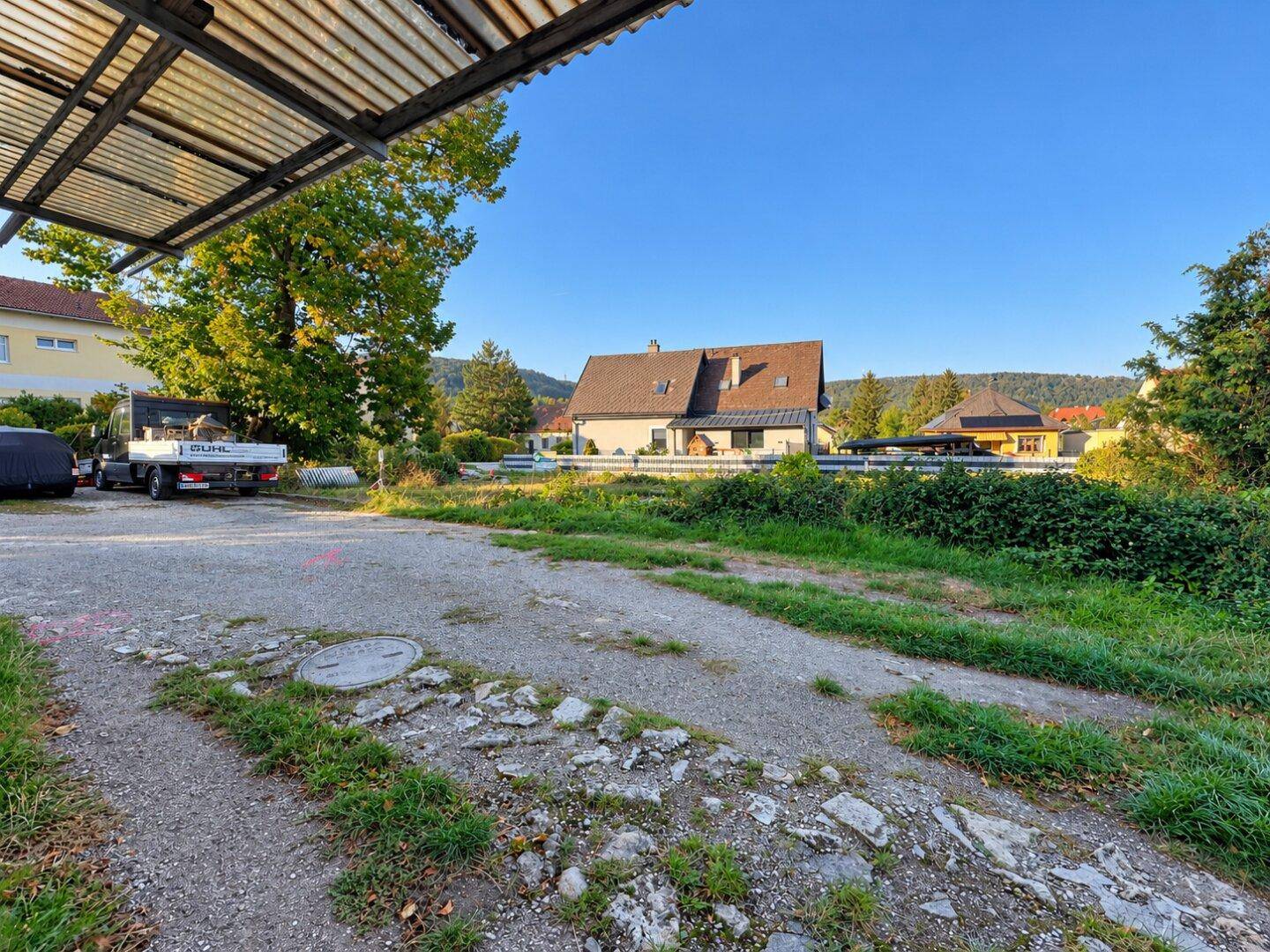 Großer Schotterparkplatz mit Blick auf die umliegende Landschaft und weitere Gebäude.