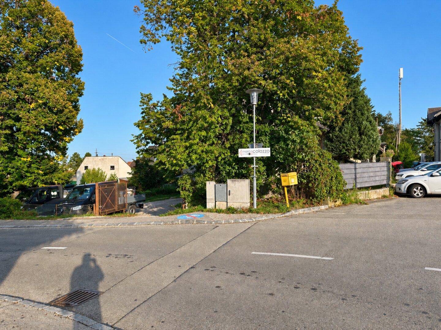 Straßenecke mit Bäumen, einem Straßenschild und Blick auf die Umgebung.