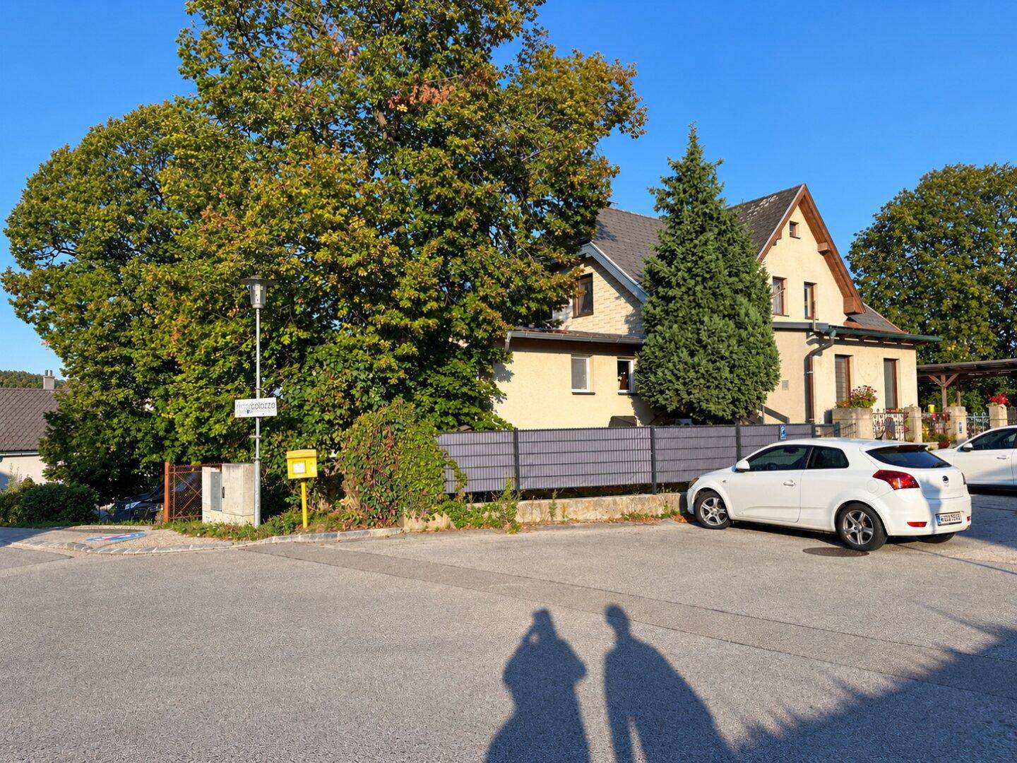 Vorderansicht des Hauses von der Straßenecke aus, mit Zaun und parkenden Autos.