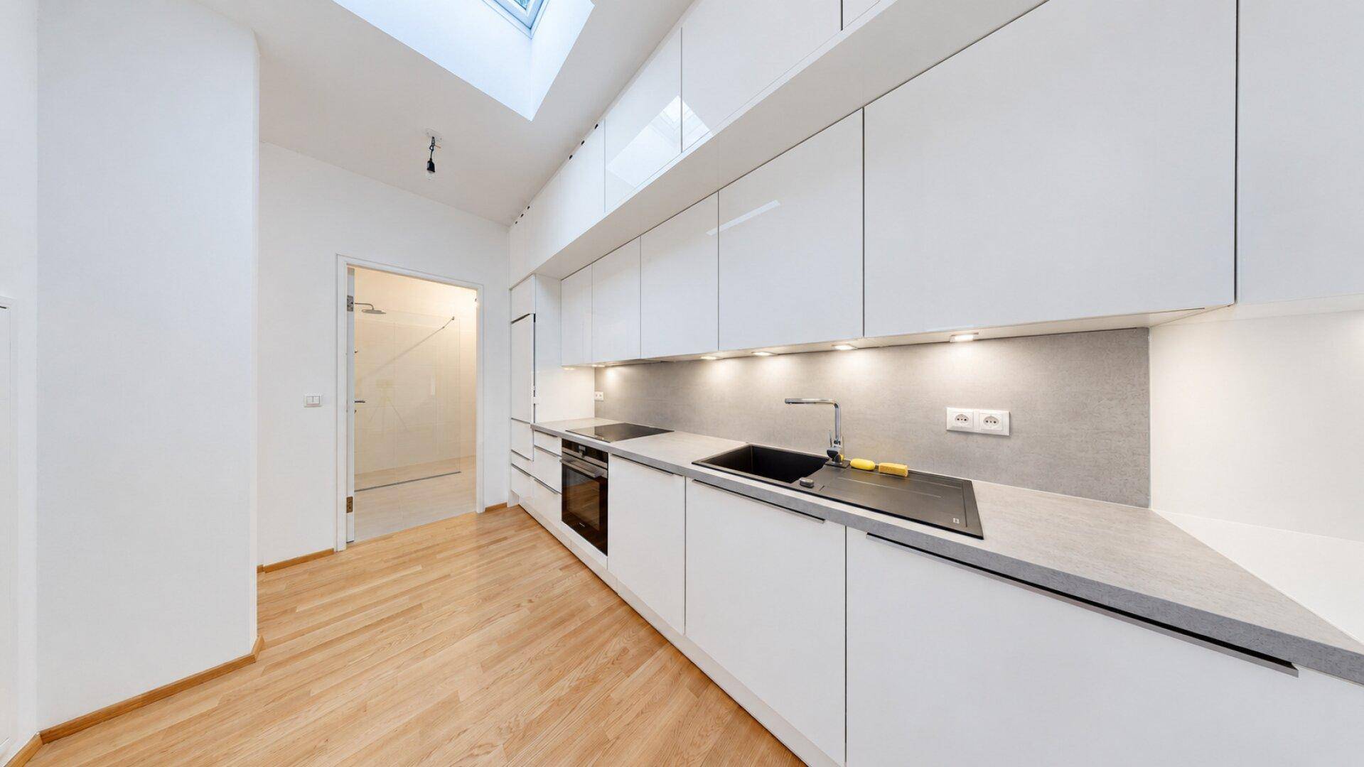 Moderne, helle Küche mit weißen Hochglanzschränken, Einbaugeräten und Dachfenster.