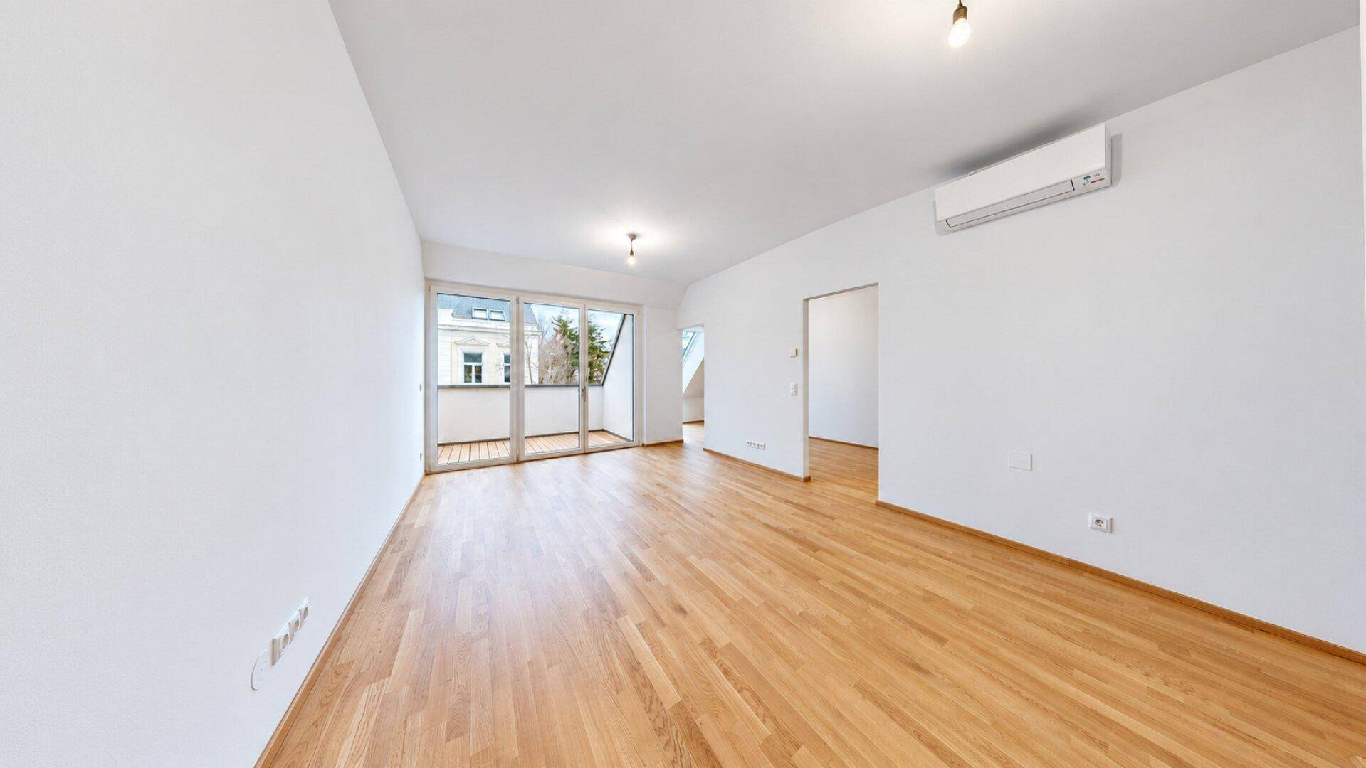 Geräumiges, helles Wohnzimmer mit Holzboden, Balkonzugang und Klimaanlage.