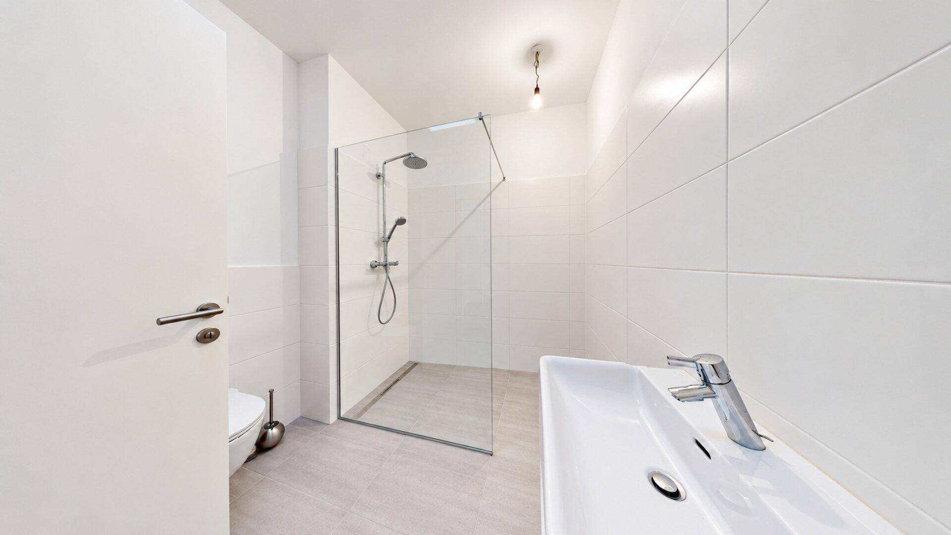 Modernes Badezimmer mit weiß gefliesten Wänden, begehbarer Dusche und Einzelwaschbecken.