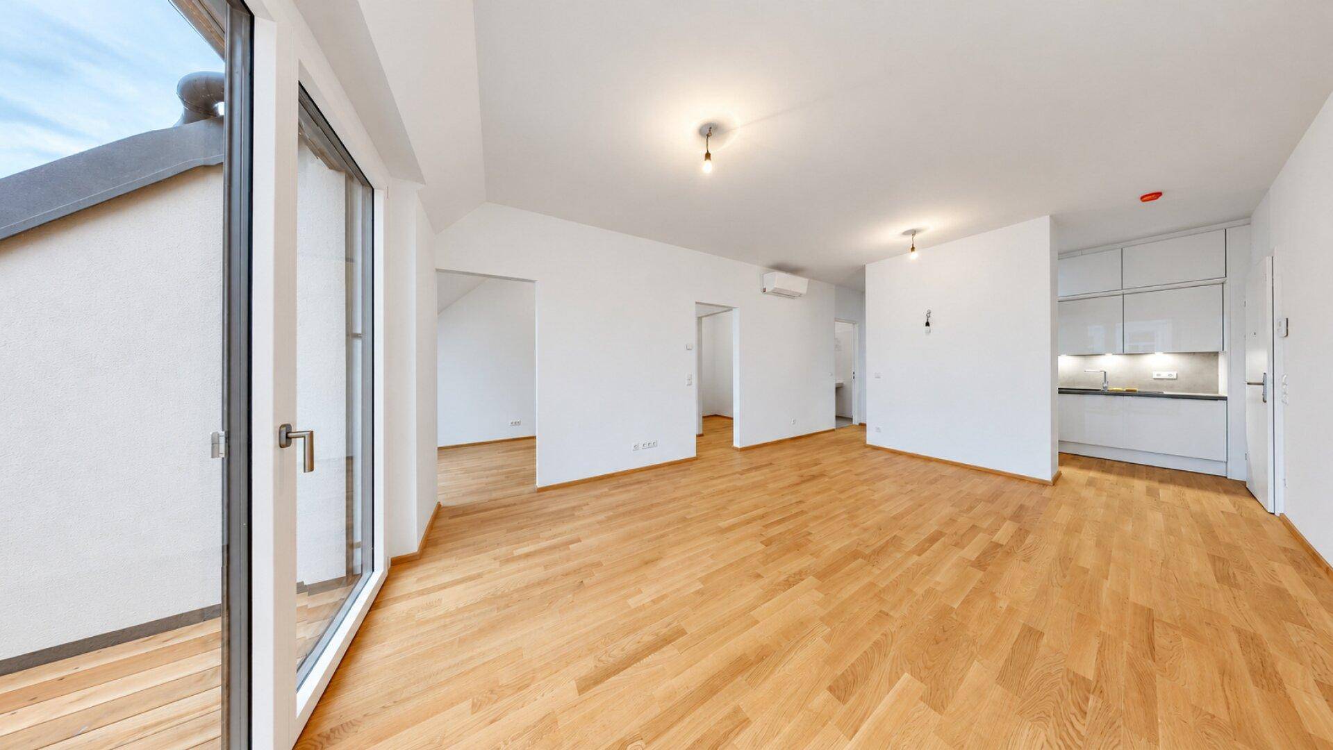 Heller Wohnbereich mit Holzboden und großem Fenster, das zu einem Außenbereich führt.