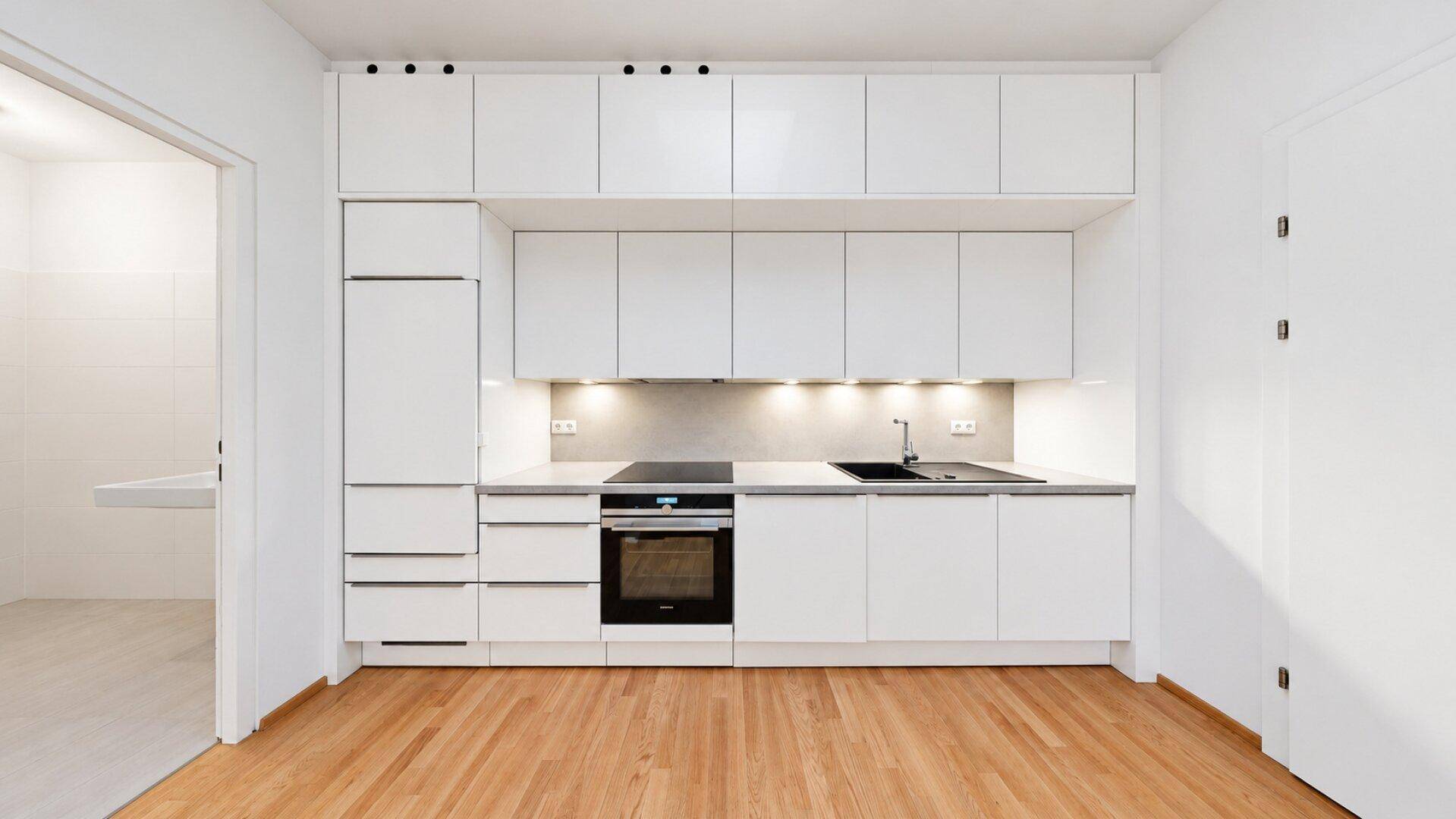 Moderne Einbauküche mit weißen Schränken, integrierten Geräten und Holzboden.