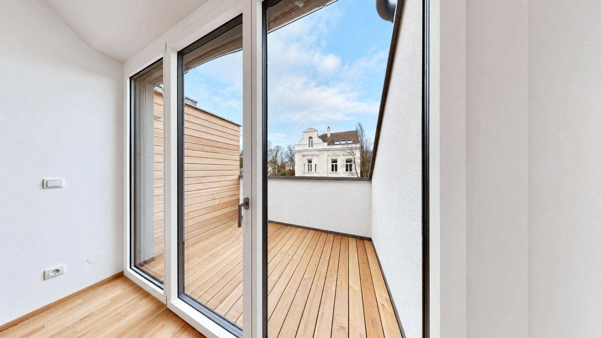 Heller Balkon mit Holzfußboden und Blick auf die umliegenden Gebäude.
