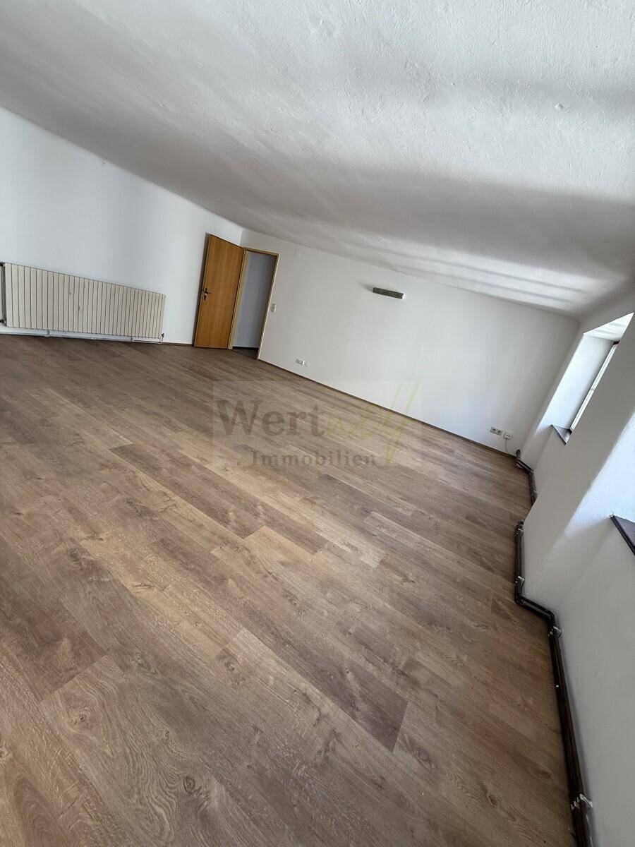 Heller Dachbodenraum mit Laminatboden, Heizkörper und einer Holztür.