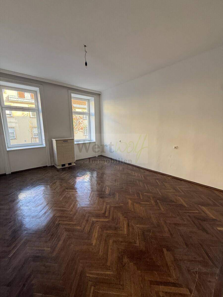 Helles Zimmer mit klassischem Fischgrätparkett und zwei großen Fenstern zur Straßenseite.