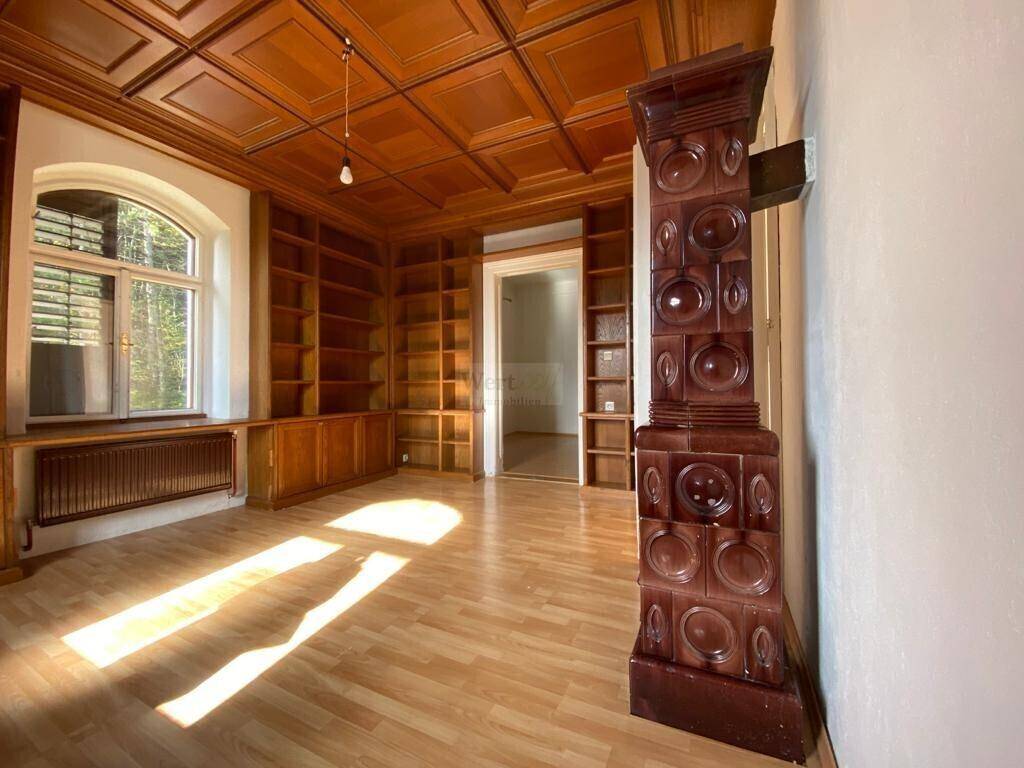 Großer Raum mit Holzkassettendecke, eingebauten Bücherregalen und einem traditionellen Kachelofen.