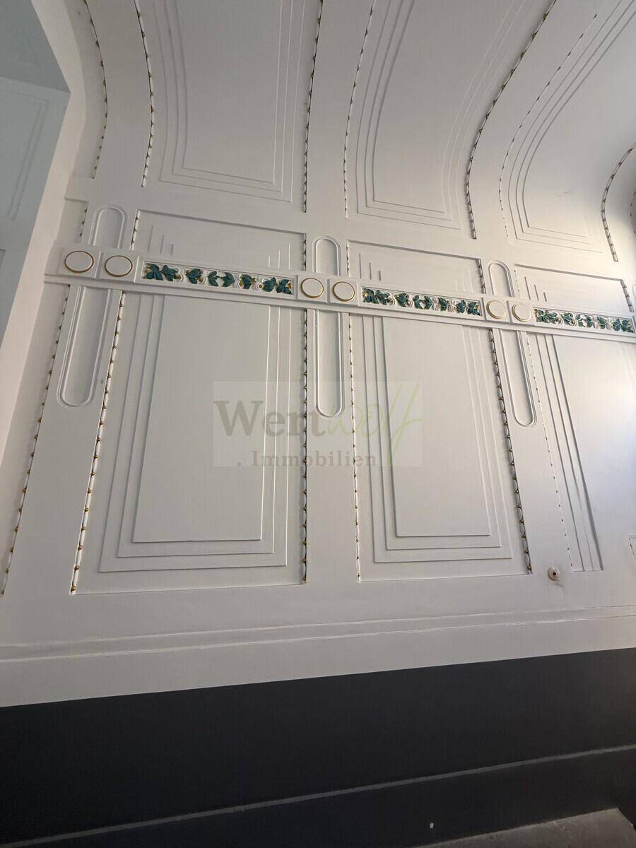 Nahaufnahme der kunstvollen Wandgestaltung im Flur mit Stuckelementen und grünen Akzenten im Jugendstil.