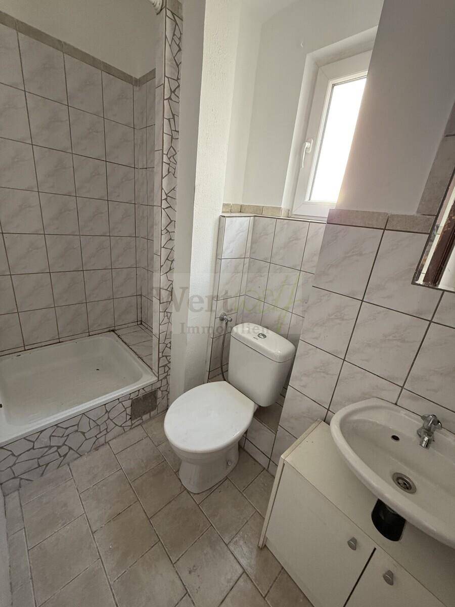 Helles Badezimmer mit Dusche, WC, Waschbecken und Fenster für Tageslicht.