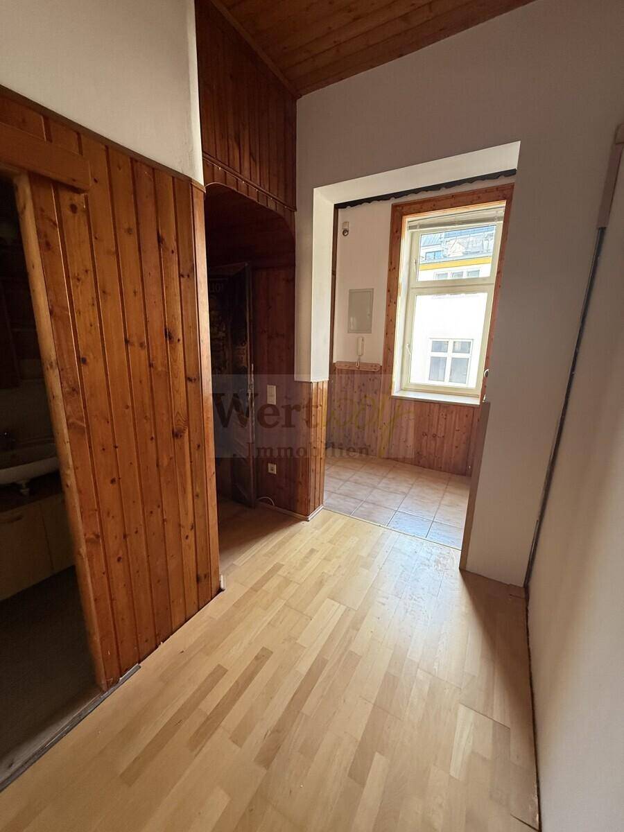 Flur mit Holzvertäfelung und Parkettboden, der zu einem hellen Bereich mit Fenster führt und eine gemütliche Atmosphäre schafft.