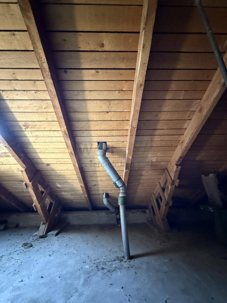 Unausgebauter Dachboden mit sichtbarer Holzkonstruktion und Rohren.