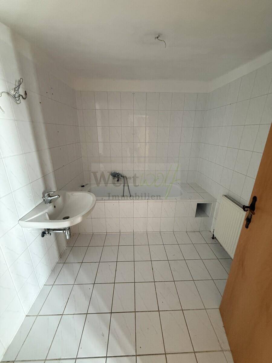 Badezimmer mit weißen Fliesen, Badewanne und Waschbecken, bereit zur Modernisierung.