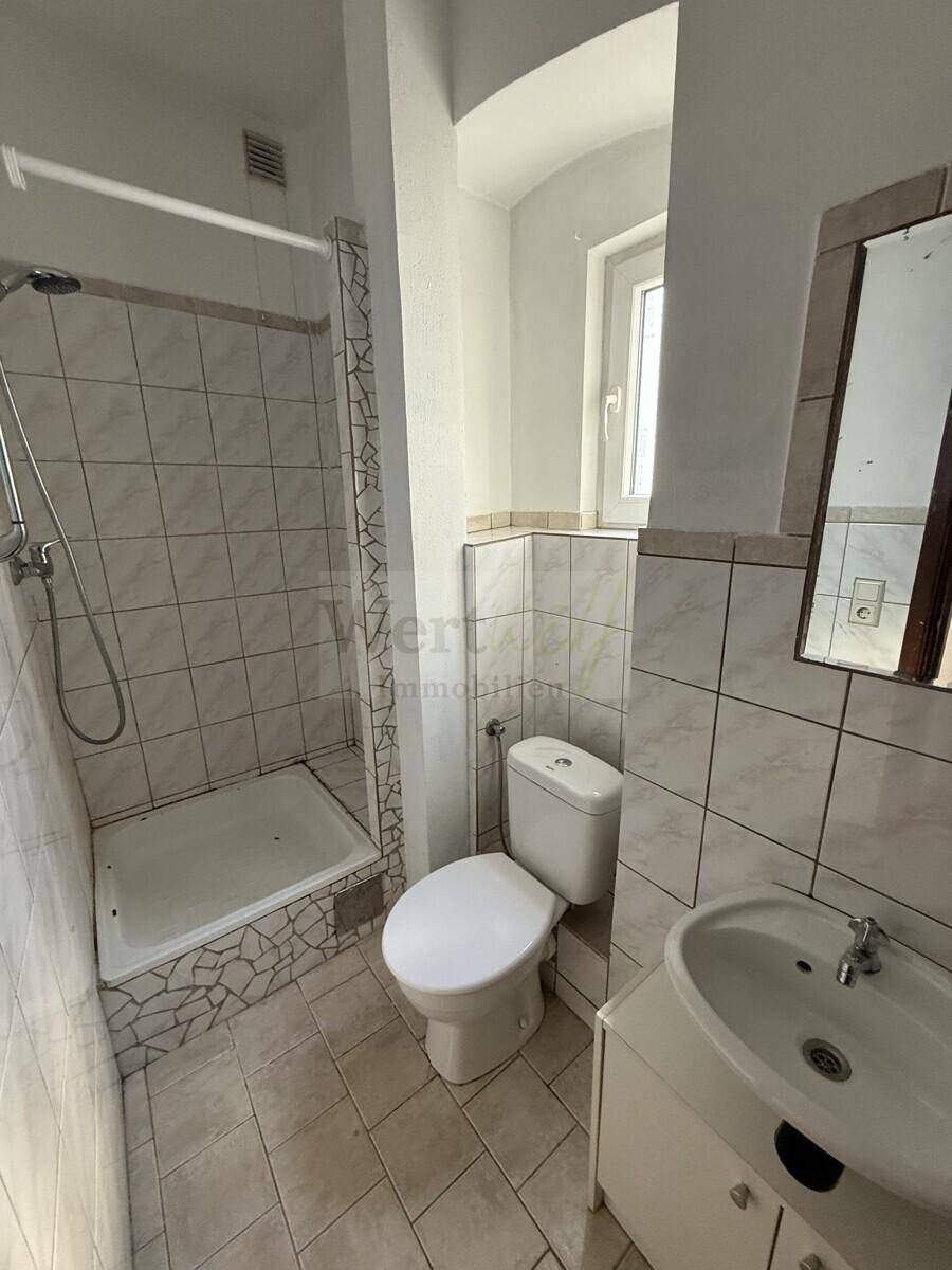 Badezimmer mit Duschbereich, WC, Waschbecken und Fenster für Tageslicht.