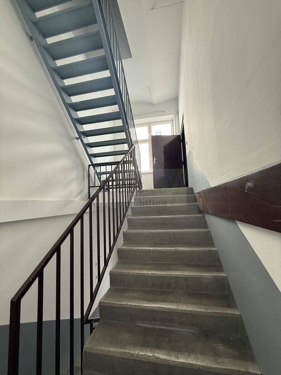 Treppenhaus mit robusten Betonstufen und Metallgeländer, das zu den oberen Etagen führt.