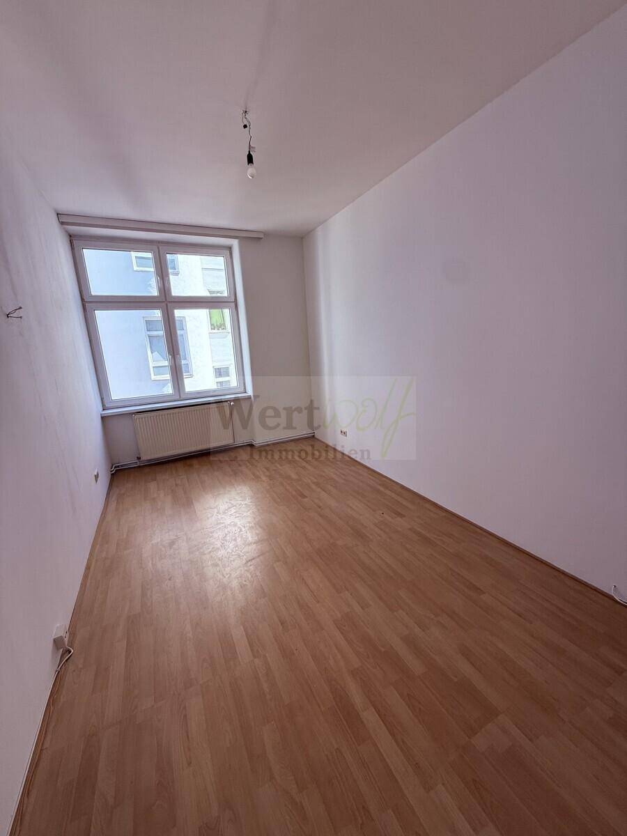 Leeres Schlafzimmer mit hellem Laminatboden und einem Fenster mit Blick auf die Umgebung.