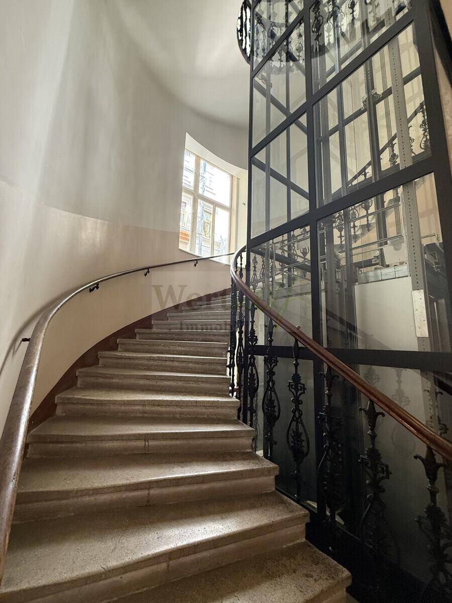 Historische Wendeltreppe mit schmiedeeisernem Geländer und modernem Glasaufzug.