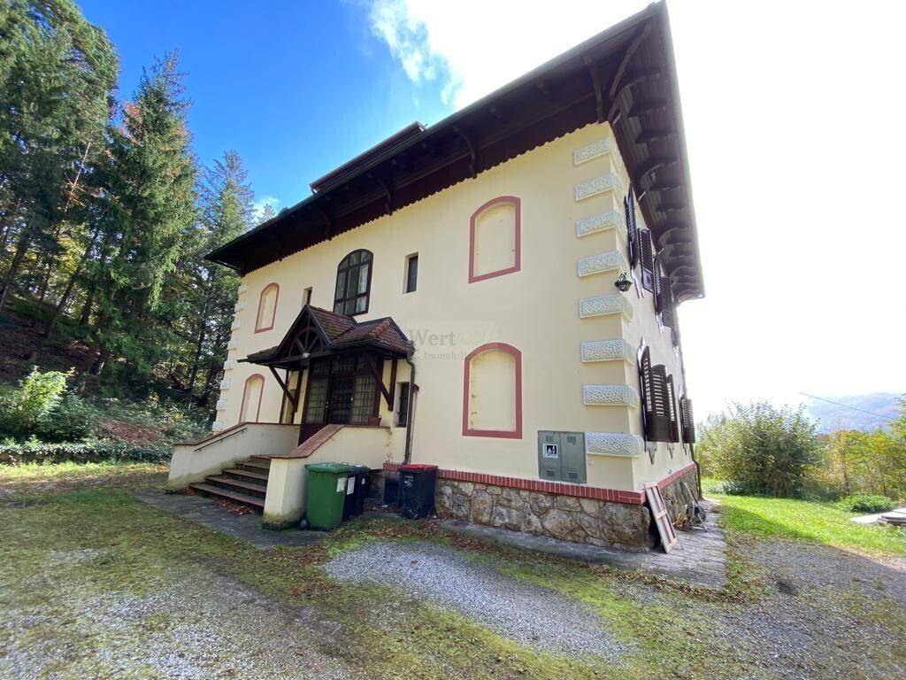 Seitenansicht des historischen Gebäudes mit traditioneller Fassade, Steinmauerwerk und grüner Umgebung.