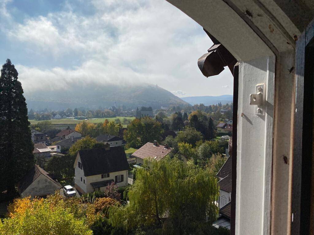 Breiter Ausblick über die Dächer der Häuser, grüne Landschaft und ferne Berge.