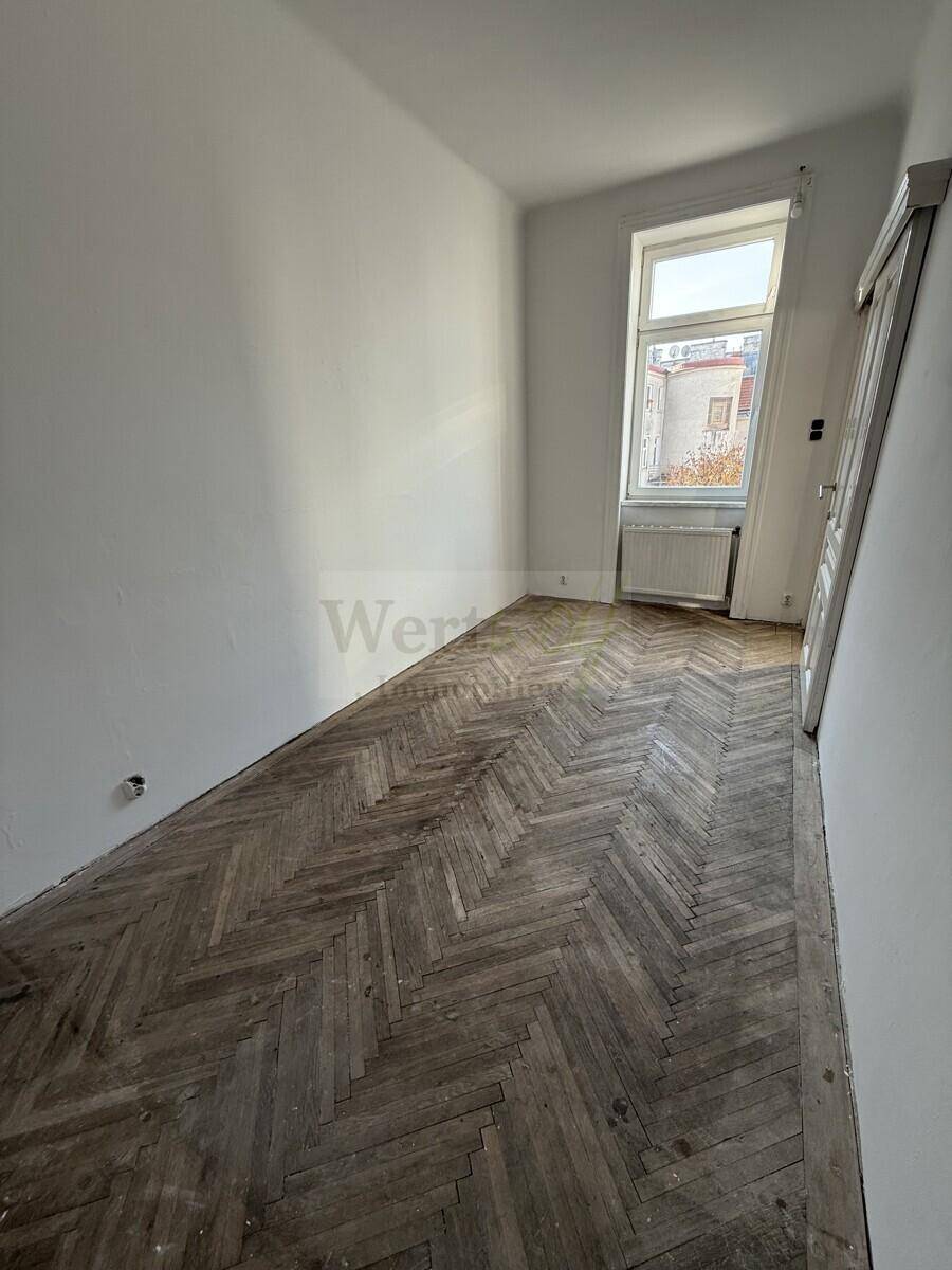 Kleineres Zimmer mit Fischgrätparkettboden und einem Fenster, das auf einen Innenhof blickt.