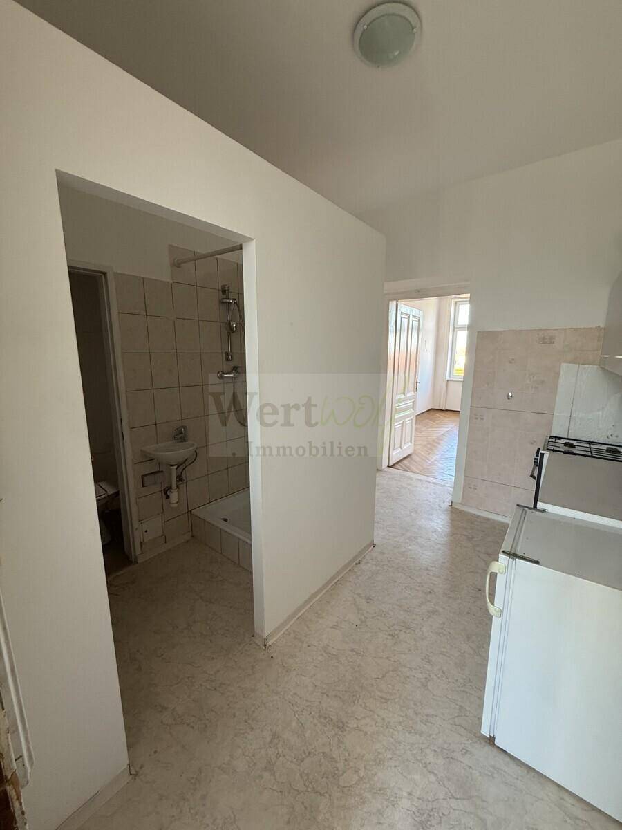 Flur mit Fliesenboden, der zu einem Badezimmer und einer Küche führt.