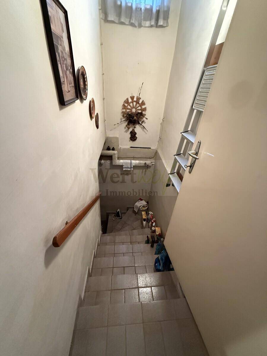 Treppenhaus mit Fliesenboden und Holzgeländer, das in den Keller führt.