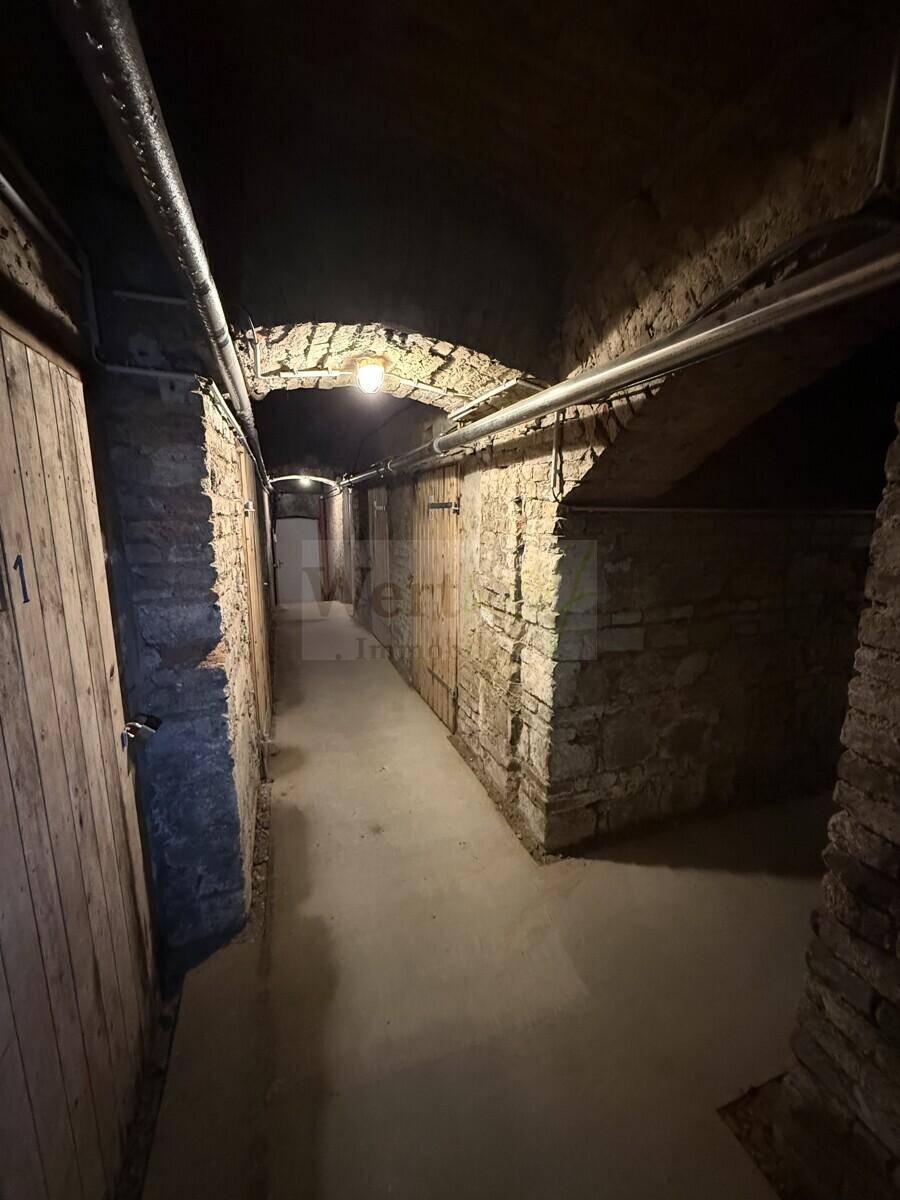 Gewölbter Kellergang mit Steinmauern und Holztüren zu den einzelnen Abteilen.