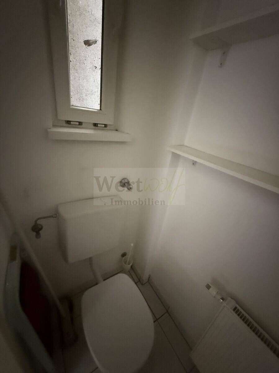 Separate Toilette mit Fenster und Fliesenboden, die eine einfache Ausstattung aufweist.