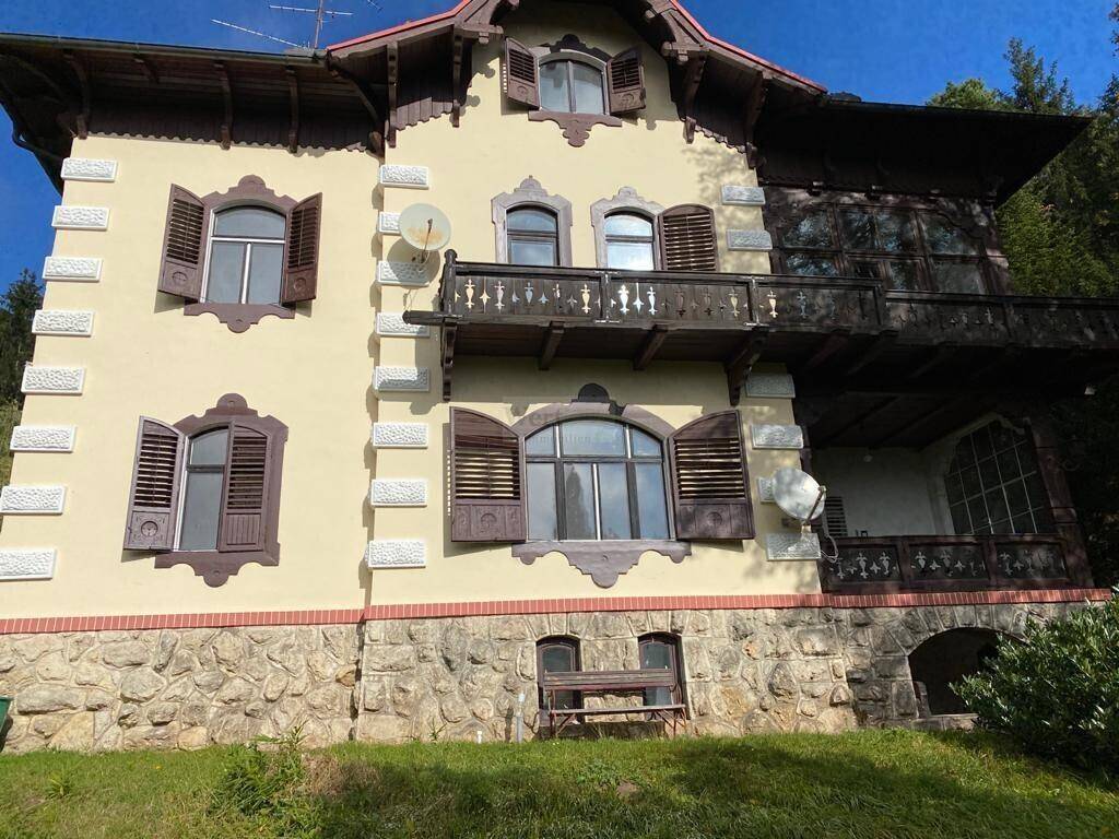 Detailansicht der historischen Fassade mit Steinmauerwerk, Holzbalkonen und verzierten Fensterläden.