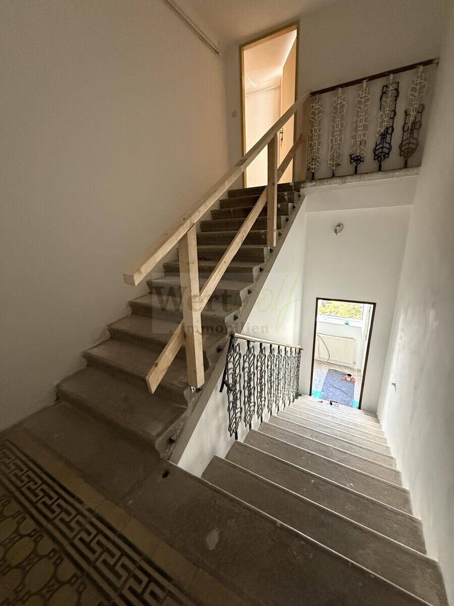 Treppenhaus mit Steinstufen und dekorativem Metallgeländer, das zu den oberen Etagen führt.