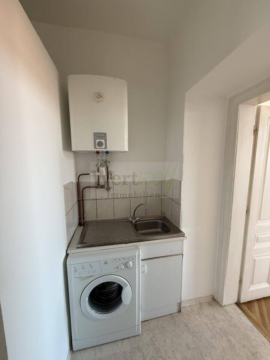 Kleiner Hauswirtschaftsraum mit Waschmaschine, Spülbecken und Warmwasserboiler.
