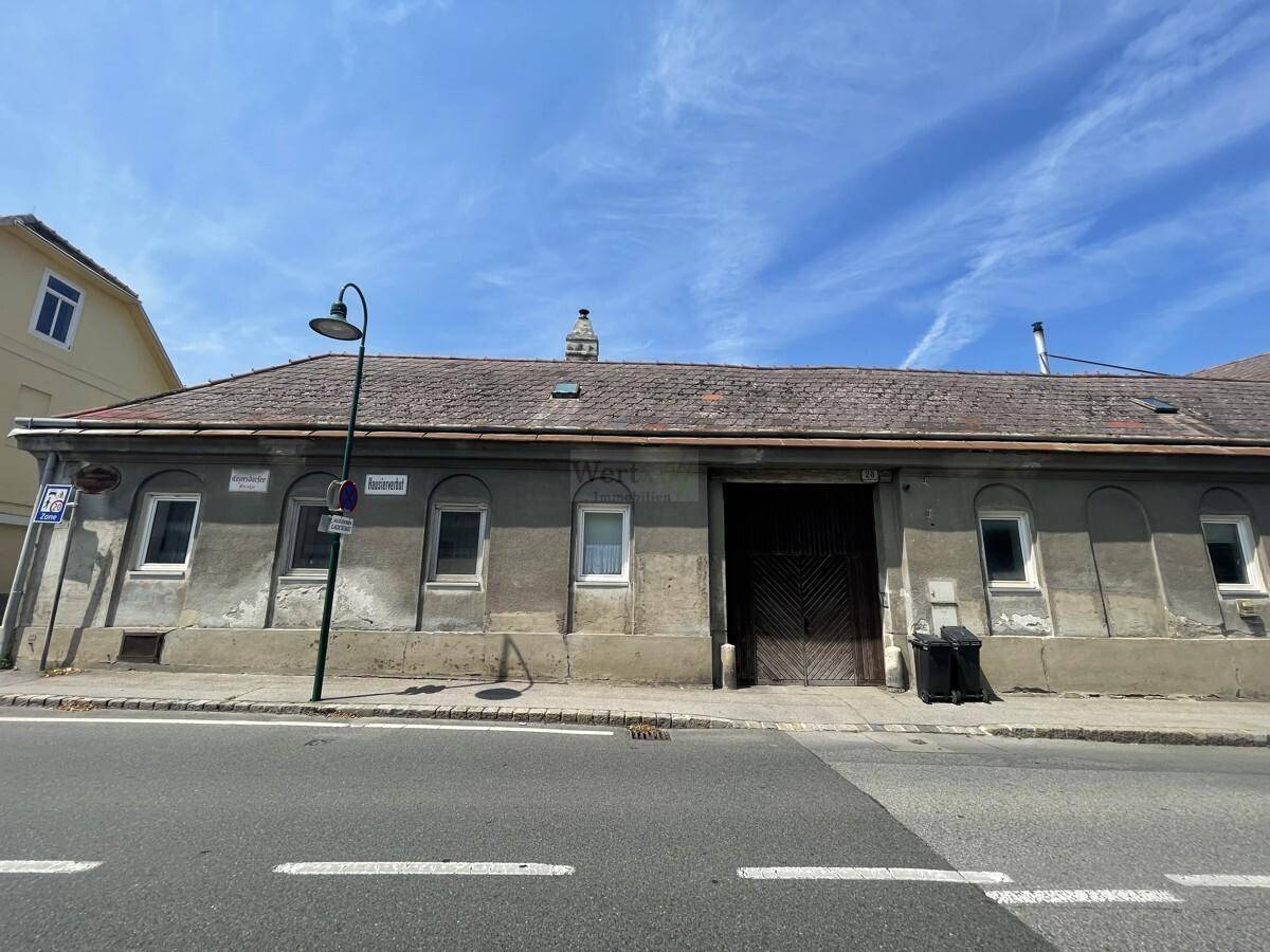 Lange Fassade eines alten Gebäudes direkt an der Straße mit mehreren Fenstern und einem großen Tor.