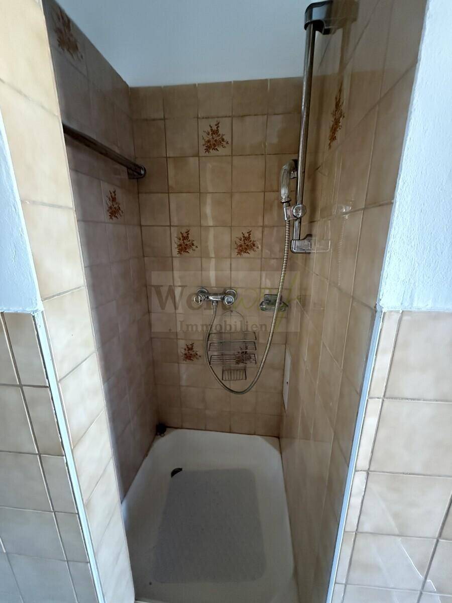 Kleines Badezimmer mit Duschwanne und älteren Fliesen, das eine dringende Modernisierung erfordert.