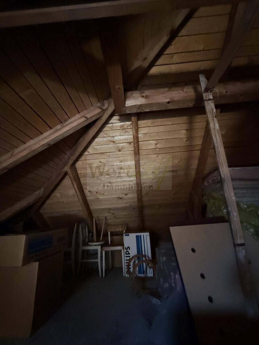 Dunkler Dachboden mit sichtbarer Holzkonstruktion und gelagerten Gegenständen.