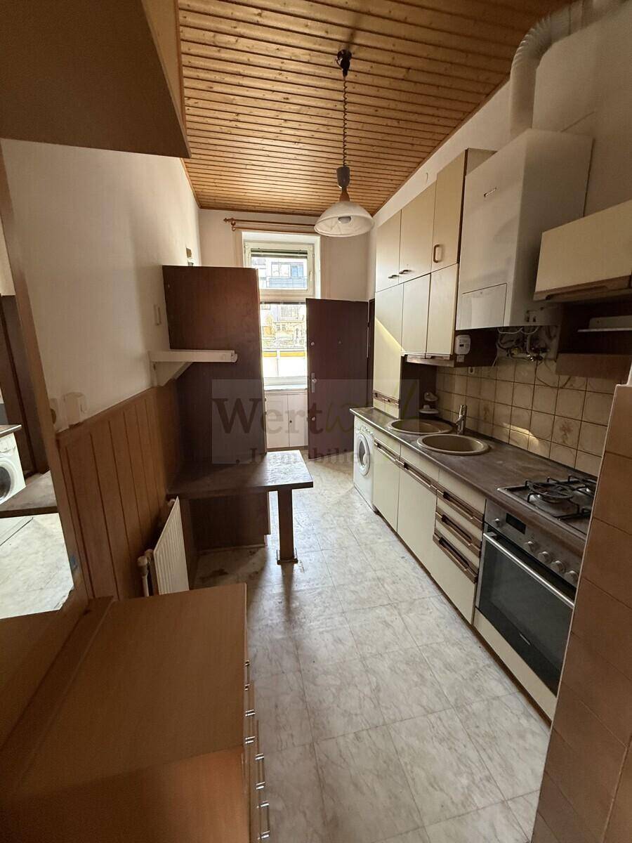 Ältere Küche mit Holzdecke, Einbauschränken und Gasherd, die eine umfassende Renovierung benötigt.